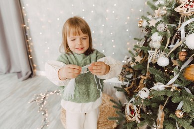 little girl decorates the christmas tree with toys. a cute baby is preparing at home for the celebration of christmas.