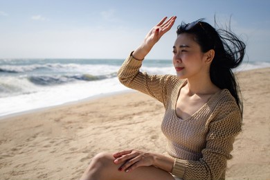 beautiful asian woman with sunglasses sitting under strong sunlight on beach, sun uv protection or skincare concept