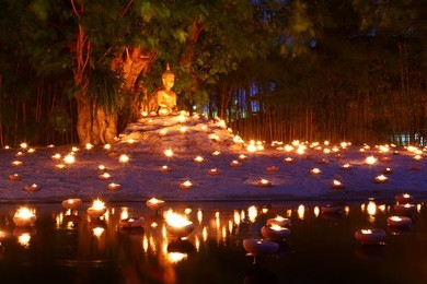 buddhist monk fire candles to the buddha with beautiful water reflection in phan tao temple, chiangmai, thailand 