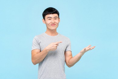 portrait of happy young asian man pointing finger to empty space in isolated blue studio background