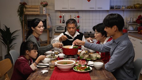 asian extended family blowing and tasting the hot delicious soup with spoons while they are gathering together for new year's reunion meal at home in the evening