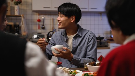 selective focus of hungry asian adult male father reaching for delicious food and burning his mouth while eating reunion dinner with family on chinese new year's eve at home