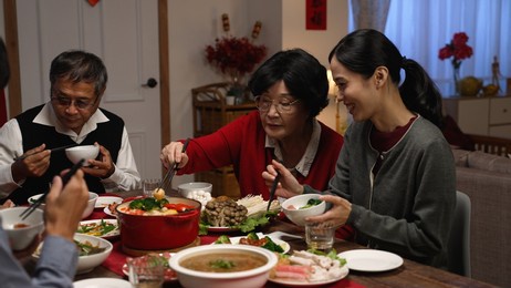 happy asian grandmother and daughter in law giving food to each other while eating dinner together on the eve of chinese new year at a cozy home interior.