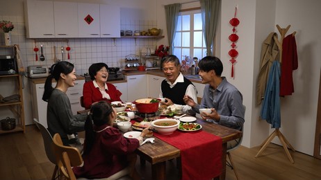 happy asian extended family laughing at the man's joke while having reunion dinner on chinese new year's eve in a cozy festive home interior