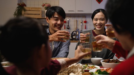 selective focus of happy young asian couple drinking toast with tea to their family at chinese lunar new year reunion dinner at home