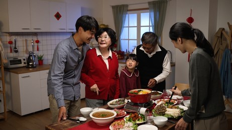 cheerful asian senior mother in red clothes talking to her son while daughter in law preparing hot pot with chopsticks at dining table. getting ready for lunar new year reunion dinner