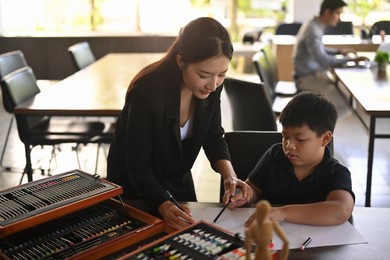 smiling asian teacher helping children coloring picture in art class