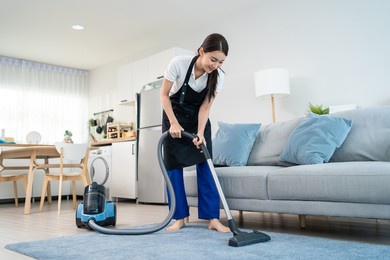 asian cleaning service woman worker cleaning in living room at home. beautiful young girl housekeeper cleaner wear apron and vacuuming messy dirty floor for housekeeping housework and chores in house.