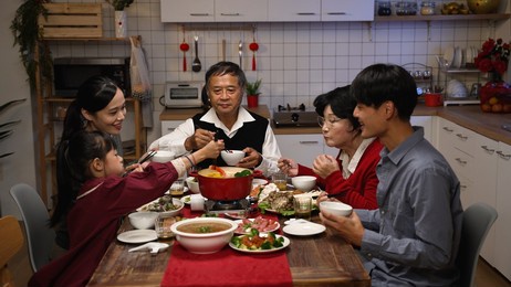 happy asian family members picking food from hot pot with chopsticks while enjoying traditional reunion dinner at home on chinese new year's eve