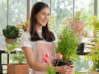 portrait beautiful woman smiling asian bastard thai-chinese long black hair wearing white t-shirt. pink apron with hand holding small tree basket inside room, arranged in white beautiful happy relax
