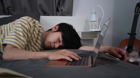 tired young asian man sleeping on bed near computer laptop.