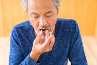 asian elderly man takes medicine capsules