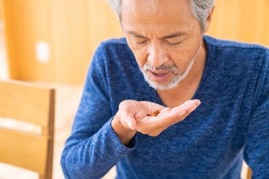 asian elderly man takes medicine capsules