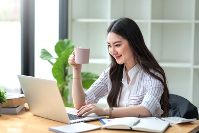 beautiful young asian businesswoman drinking a coffee working on laptop at office.