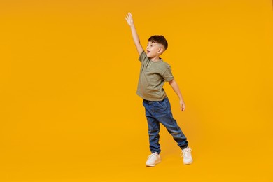 full body side view little small smiling happy boy 6-7 years old wear green t-shirt walk go waving hand isolated on plain yellow background studio portrait. mother's day love family lifestyle concept
