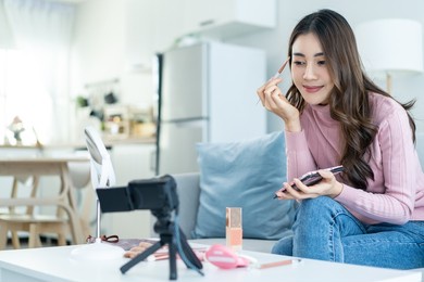 asian professional woman artist stay home, enjoying makeup herself. young attractive beautiful girl sit on sofa, feel happy look to mirror and coloring eyebrows on face enjoy beauty cosmetic in house.