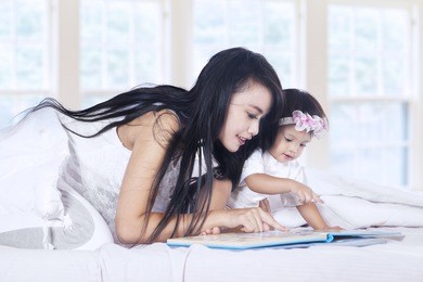 close-up of a mother and baby girl reading book story on bed