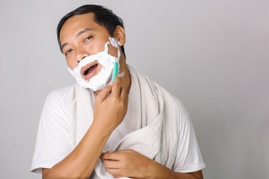 handsome asian man shaving. handsome asian man shaving his face and looking at camera while standing on grey background