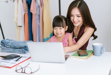 beautiful female entrepreneur. young asian mother with daughter using laptop computer and checking order for delivery to customer. startup small business owner, freelance work and new normal concept