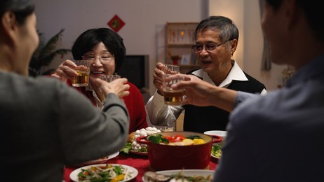 over shoulder shot with selective focus senior couple grandfather and grandmother making toast to family members, celebrating spring festival while having big meal on new year's eve