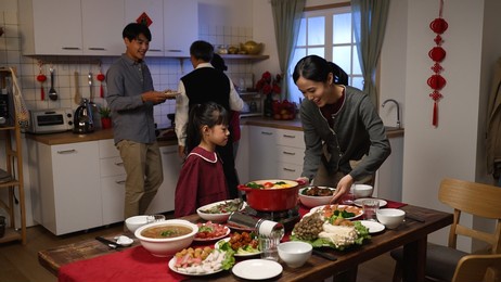 happy grandfather talking to little girl granddaughter by dining table and looking at other family members working together preparing for chinese new year's dinner party at home