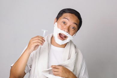 handsome asian man shaving. handsome asian man shaving his face and looking at camera while standing on grey background
