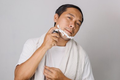 handsome asian man shaving. handsome asian man shaving his face and looking at camera while standing on grey background