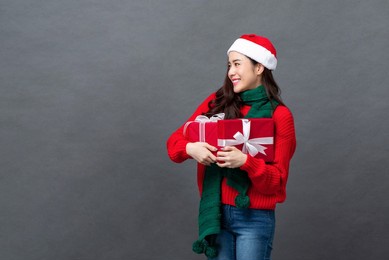 portrait of happy beautiful asian woman in christmas attire holding red gift boxes smiling and looking sideways on gray isolated studio background