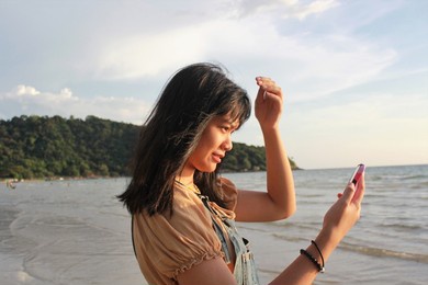 asian girl with black hair calling video conference  by phone at the beach with sunshine in sunset time.