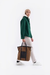 full body young man wearing a white hoodie with green shirt with hat holding handbag walking in studio

