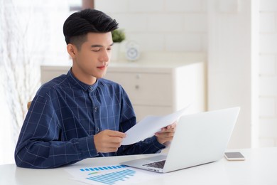 young asian business man looking document data graph and chart paper, marketing and investment, report of statistics profit for financial, economic and growth of finance, management and planning.