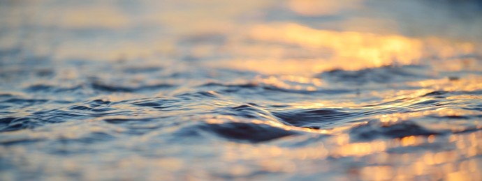 sea shore at sunset, close-up. pebbles, storm waves. abstract background, details blurred in bokeh. blue, yellow, orange, pink colors. soft sunlight, golden hour. peace, meditation, tranquility themes