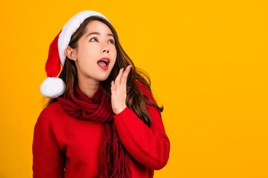 smiling, excited and shocked asian woman wearing christmas sweater and christmas hat on yellow wall with copy space.