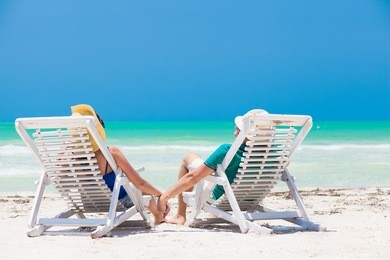 happy young couple suntanning on beach chairs ot tropical mexico beach