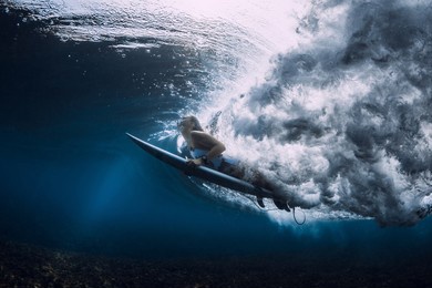 surfer woman with surfboard duck dive under wave in ocean.