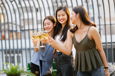 three beautiful asian women partying in rooftop bar and toasting drinks at sunset. happy young people enjoying drinks on rooftop in evening. concept about women night out.