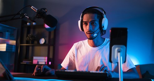 young confident asian man playing online computer video game, colorful lighting broadcast streaming live at home. gamer lifestyle, e-sport online gaming technology concept