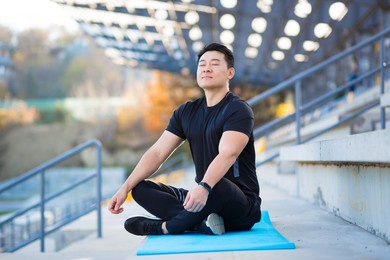 handsome asian man meditating in modern urban stadium, sitting lotus pose male practicing yoga mat, zen. relaxes outdoors in nature in the morning concept healthy lifestyle, relax, calm, meditation