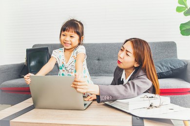 mother is tired of her daughter naughtyness concept : mother working on business paperwork encounters the aches and pains of her young daughter's mischief playing on her laptop as she sits at work.