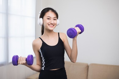 attractive asian young fitness woman lifting dumbbell weights workout at home in living room. fresh feeling female training and exercise wearing sport wear fit body.