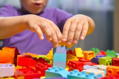a beautiful boy is playing at home with building blocks. a cute smiling boy is playing with a constructor with a lot of colorful plastic blocks in the room, building a city. preschool classes.