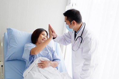 the doctor encouraged ready to touch the hand of a female patient who is giving saline solution on the patient's bed.