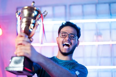excited gamer celebrating win by showing trophy to audience and shouting by looking at live streaming camera during esports tournament - concept of professional champion gamer