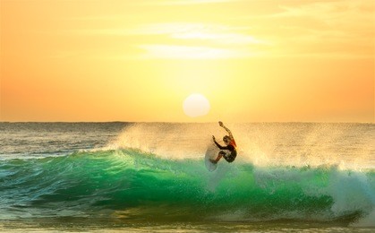 surfing on a green wave with sun rising in the background