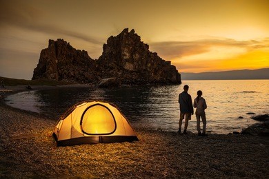 couple stand at tent and baikal lake shore and looking at the sunset