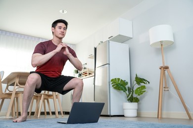 asian attractive young man doing exercise using laptop in living room. handsome male in sport cloth follow exercise or yoga instruction video online trainer workout at home. healthy lifestyle concept.