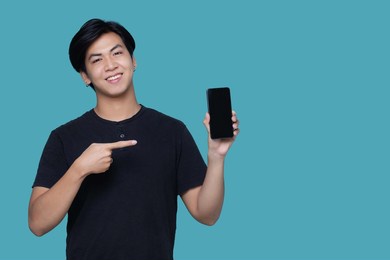 asian smart young man pointing finger to smart phone screen and standing isolated on blue color background with copy space.
