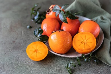 whole and cut persimmon fruit with water drops and green leaves on green concrete background.