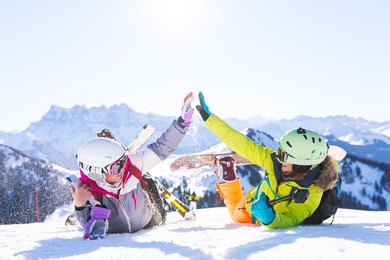 two female friends with ski and snowboard equipment having fun and high five with snow in the air.