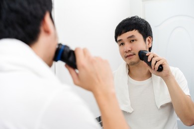 man using electric shave to shaving his face in the bathroom mirror